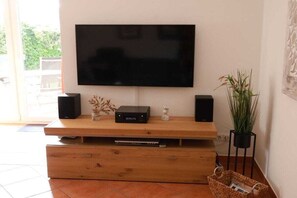 Ein Flachbildfernseher an einem Holzboden, Lautsprecher, ein kleines dekoratives Objekt und eine Pflanze.