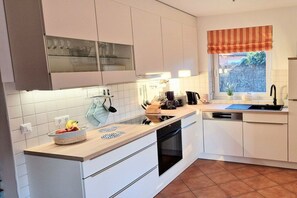 A modern kitchen with white cabinetry, a wooden countertop, a built-in oven, and a window with a striped valance. - Holiday apartment with 1 bedroom (Borkum)