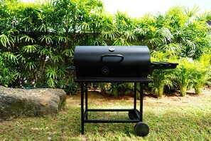 A portable barbecue grill on a wheeled cart in a garden with lush green foliage.