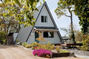 Ein Haus mit einem Giebeldach, einer Veranda und einem Garten mit verschiedenen Pflanzen und Blumen.