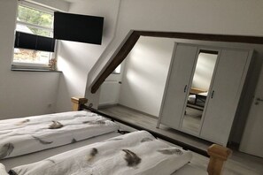 A bedroom with a sloped ceiling, a bed with a feather pattern, a wardrobe, and a television mounted on the wall. - Holiday home Am Meinweg (Wassenberg)