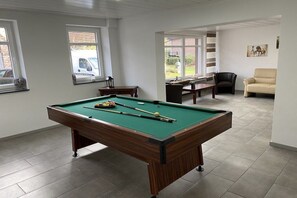 A pool table in a room with a sofa, a chair, and a window with a view of the outside. - Holiday home Am Meinweg (Wassenberg)