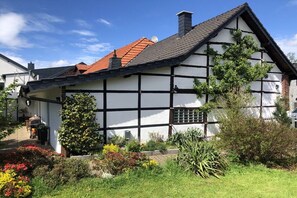 A traditional half-timbered house with a sloped roof, surrounded by a well-maintained garden with various plants and flowers. - Holiday home Am Meinweg (Wassenberg)