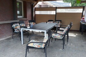 Um pátio externo com mesa e cadeiras, parede de tijolos e cerca de madeira.
