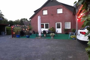A red brick house with a green lawn, outdoor seating, and a white car parked nearby. - Holiday home with 2 bedrooms (Butjadingen-Stollhamm)
