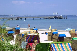 A beach with rows of beach chairs and umbrellas, a pier in the background, and a clear sky. - Holiday apartment with 1 bedroom (Sierksdorf)