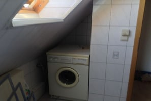 A compact laundry room with a washing machine, a skylight, and tiled walls. - Holiday home with 1 bedroom (Wurster Nordseeküste)
