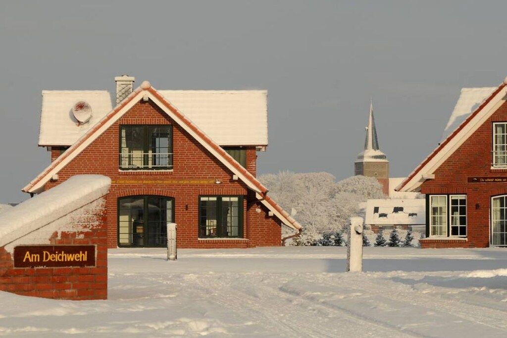 En murbygning med et skilt, der viser 'Am Deichweiler', i et snøklædt landskab.