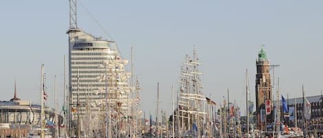 A marina with multiple sailboats docked, a prominent modern building, and a historic lighthouse.