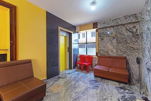 A hotel lobby with a marble floor, a yellow elevator, a brown sofa, and red chairs. - Hotel O Jayam Residency (Tirupati)