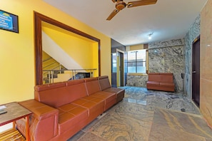A modern living room with a brown leather sofa, a ceiling fan, and a marble floor. - Hotel O Jayam Residency (Tirupati)