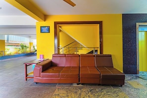 A yellow-walled room with a brown sofa, a small table, and a staircase leading to an upper level. - Hotel O Jayam Residency (Tirupati)