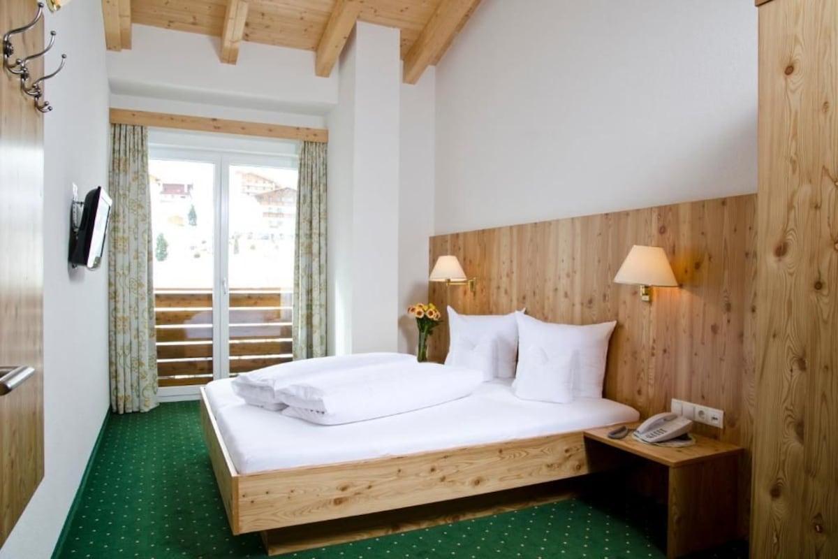 Une chambre d’hôtel avec un lit en bois, deux lampes de chevet, un téléphone et une fenêtre avec des rideaux.