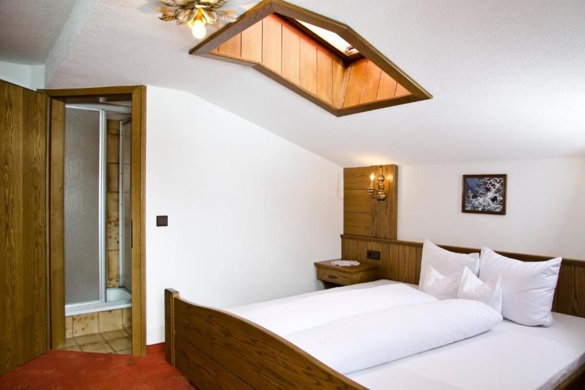 Une chambre avec un plafond en bois, un lit avec une literie blanche, une table de chevet, une armoire en bois et un tableau encadré au mur.