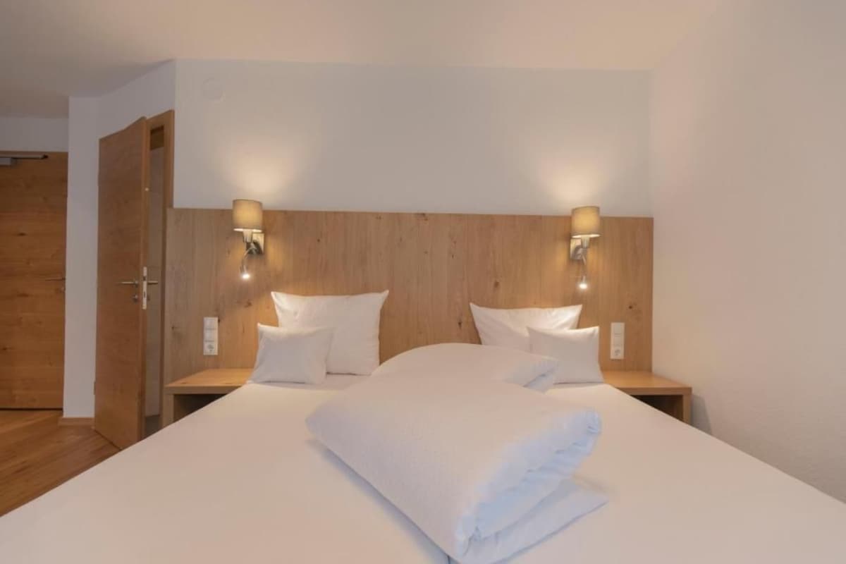 Une chambre d’hôtel avec un grand lit, deux tables de chevet et des lampes fixées au mur.