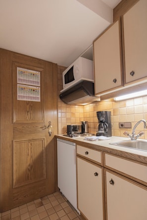 A compact kitchen with wooden cabinets, a microwave, a coffee maker, and a dishwasher. - Berghotel Rasis (Galtür)