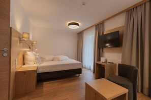 A hotel room with a bed, bedside table, chair, TV, and a small table. - Berghotel Rasis (Galtür)