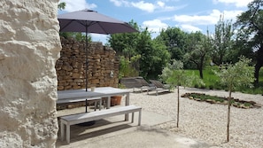 An outdoor seating area with a stone wall, a table with a bench, and an umbrella providing shade. - Holiday Home 'Numero 15' with Private Terrace, Private Garden and Wi-Fi (Autréville-Saint-Lambert)