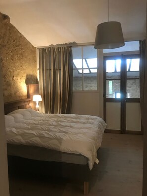 Une chambre à coucher avec un lit, une table de chevet avec une lampe, une fenêtre avec des rideaux et une vue sur l’extérieur.