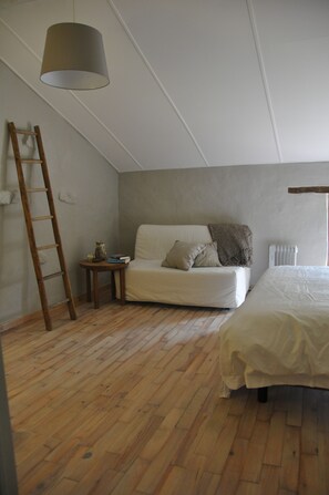 Ein Zimmer mit einem Schlafplatz in der Zwischengeschoss und einem kleinen Tisch mit Lampe, verbunden durch eine Holzleiter.
