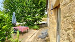 Eine Terrasse im Freien mit kariertem Tischläufer, Stühlen, einem Blumentopf und einem blauen Sonnenschirm.