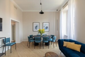 Ein modernes Wohnzimmer mit einem runden Esstisch, türkisfarbenen Stühlen, einem blauen Sofa und Kunstwerken an den Wänden.