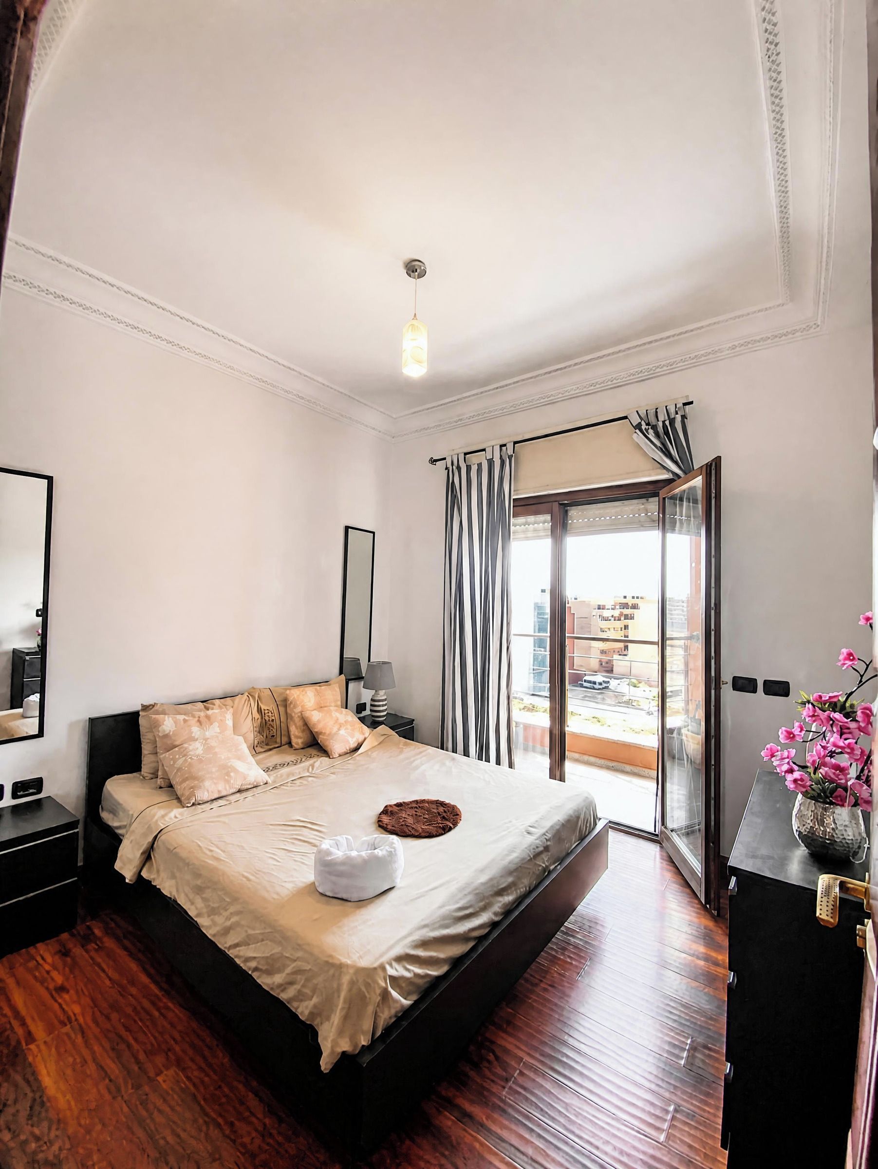 A hotel room with a large bed, a bedside table, a lamp, a window with curtains, and a view of the outside.