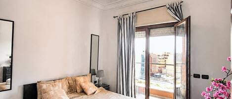 A hotel room with a large bed, a bedside table, a lamp, a window with curtains, and a view of the outside.