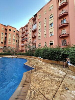 A swimming pool with a curved edge, surrounded by a concrete deck. - 2-bedroom apartment in amazing Marrakech gueliz with cool AC and Pool (Marrakech)