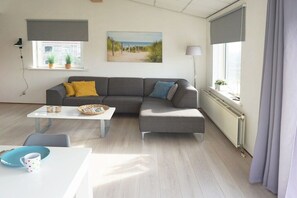 A modern living room with a gray sectional sofa, a white coffee table, and a painting of a beach scene. - Residence Juliana 19 (Julianadorp)