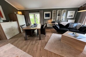 A modern living room with a dining table, black leather sofa, and a wooden coffee table. - Holiday home in Cuxhaven with swimming pool (Cuxhaven)