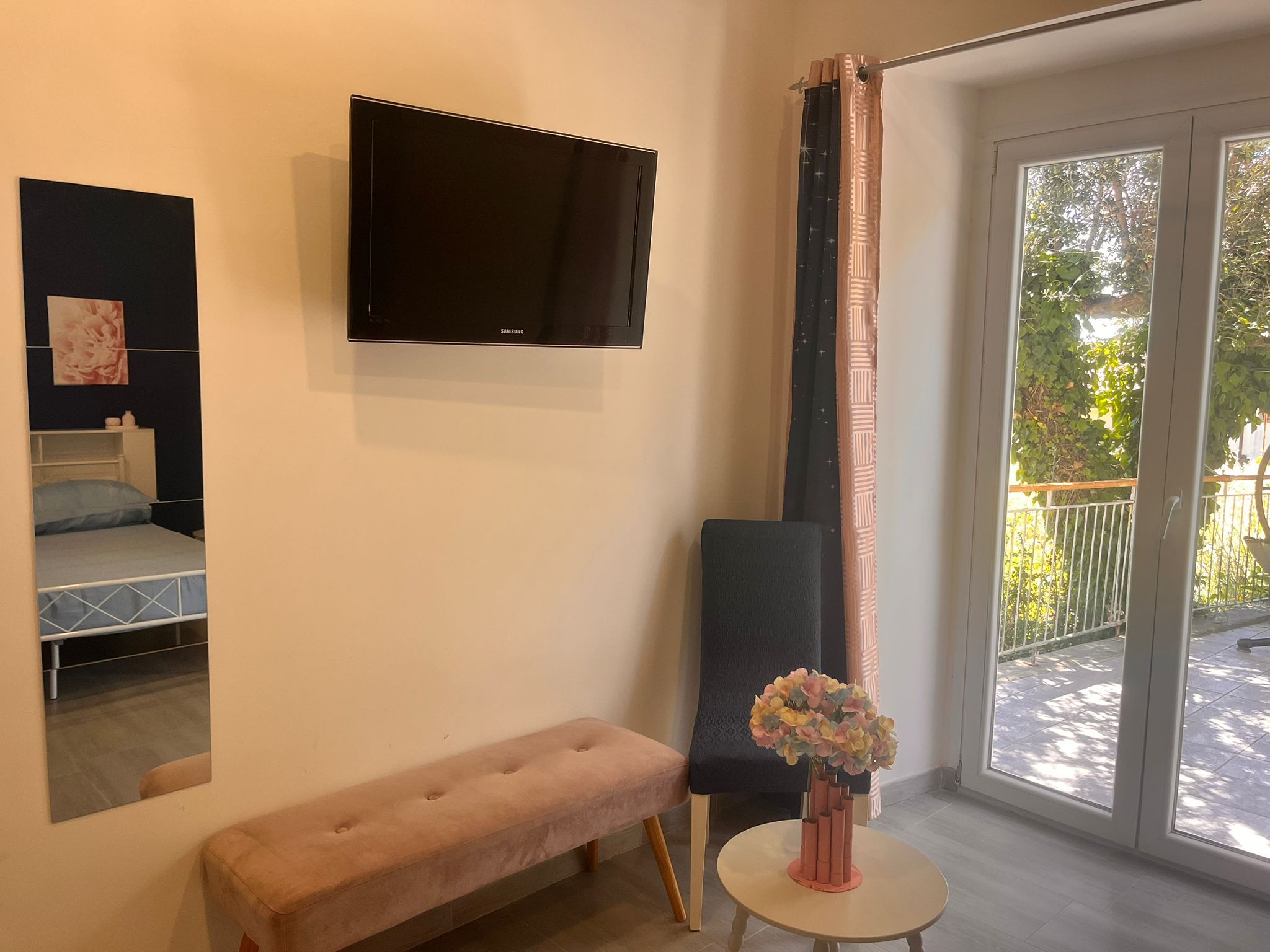Une chambre à coucher avec un lit, un banc, une télévision et une fenêtre avec des rideaux.