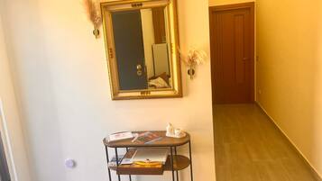 Un couloir avec un miroir, une petite table sur laquelle sont posés des livres et un vase, et une porte en bois au fond.
