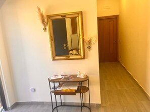 A hallway with a mirror, a small table with books and a vase, and a wooden door at the end. - A relaxing vacation home surrounded by nature, just 5 minutes from downtown, with parking (Capezzano)