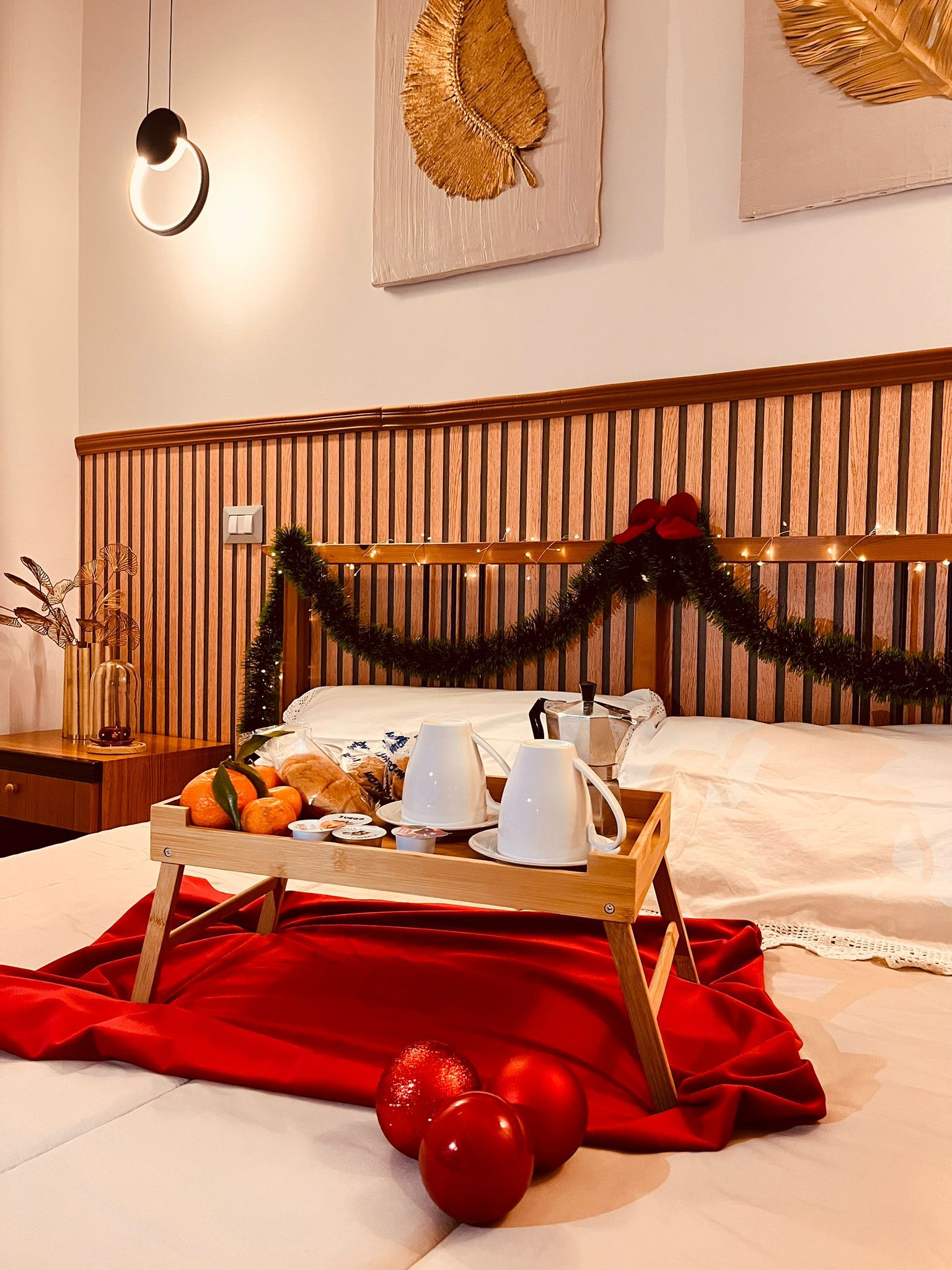 Une chambre d’hôtel avec une tête de lit en bois, une table de chevet sur laquelle se trouve un plateau avec des articles pour le petit-déjeuner, et une couverture rouge sur le lit.