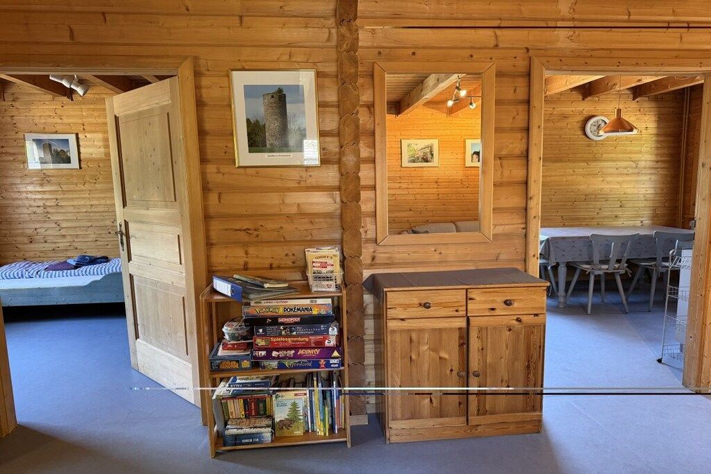 Een houten interieur met een bed, een plank met gezelschapsspellen, een kast en een eethoek met stoelen en een tafel.