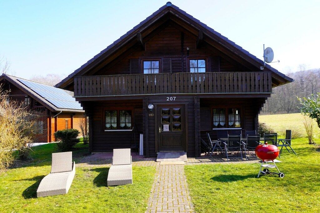 Eine zweistöckige Holzhütte mit Balkon, Hausnummer 207, und einem Grill im Garten.