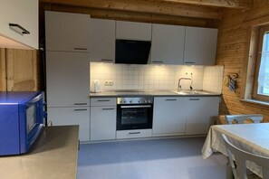 A compact kitchen with white cabinets, a built-in oven, and a microwave. - Log cabin at the Silver Lake (Frielendorf)