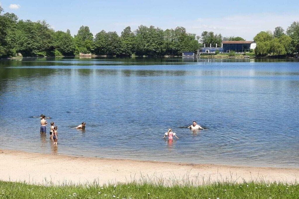 Ein See mit Schwimmenden und Menschen am Ufer.