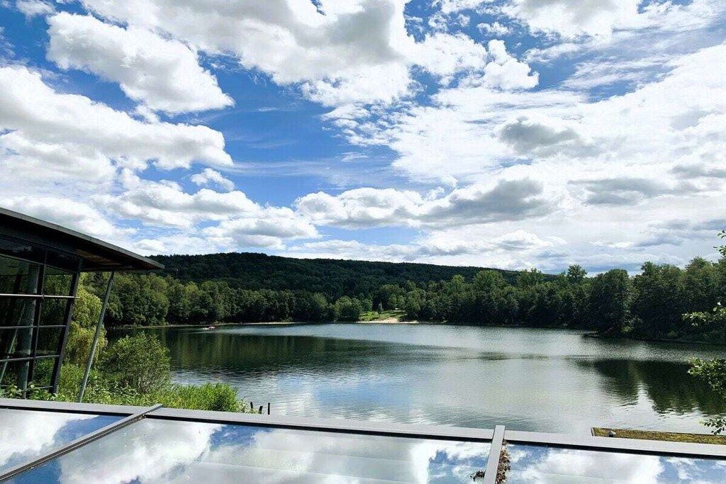 Ein Seeblick mit einer Glasstruktur, die Himmel und Wolken reflektiert.