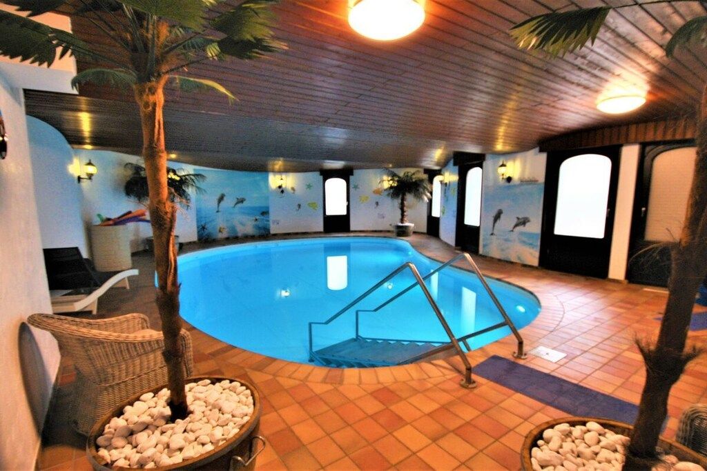 An indoor swimming pool with a wooden floor, surrounded by walls with murals, and a staircase leading into the pool.