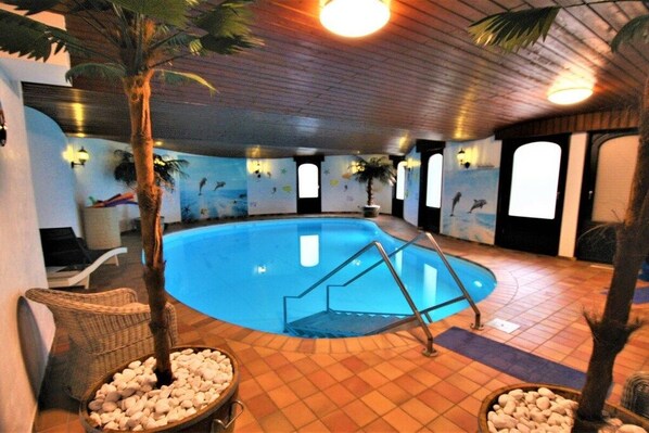 An indoor swimming pool with a wooden floor, surrounded by walls with murals, and a staircase leading into the pool.