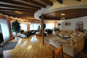 A spacious living room with wooden flooring, a large sofa set, a coffee table, and a fireplace.