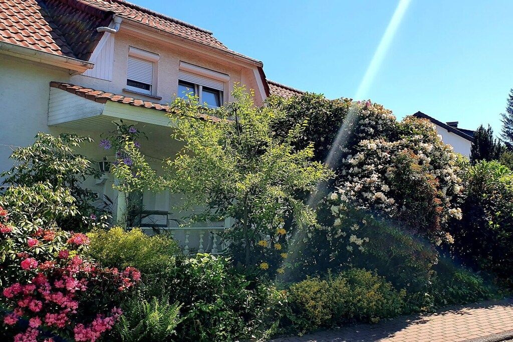 Un edificio residencial con techo de tejas, balcón y jardín con diversas plantas en flor.