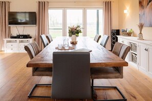 A dining area with a long wooden table, six chairs, a television, and a speaker system. - HeiDeluxe country house with sauna & alpacas (Soltau)
