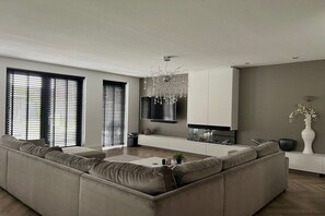 Un salon moderne avec un canapé d’angle, un téléviseur à écran plat fixé au mur et un lustre décoratif.