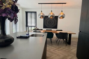 A modern kitchen with a central island, black chairs, and a hanging light fixture. - Villa in Julianadorp with barbecue (Julianadorp)