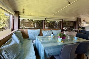 Un espace extérieur aménagé, abrité et doté de sièges confortables, avec une table pour deux personnes, des bancs rembourrés et une vue sur l’extérieur.