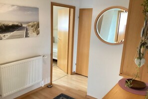 Una habitación con piso de madera, un radiador blanco, una puerta que da a otra habitación y un espejo redondo en la pared.