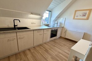 A modern kitchen with a built-in oven, a coffee maker, and a window providing natural light. - Holiday apartment with 2 bedrooms (Cuxhaven)
